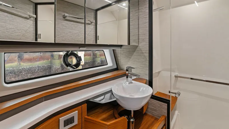 Slide: The Image of Luxurious Ensuite Bathroom This elegant ensuite bathroom on the 2025 Tiara Yachts 48LE features a sleek, modern design. The space is highlighted by a stylish vessel sink atop rich wood cabinetry, complemented by a mirrored vanity for ample storage. A spacious glass-enclosed shower - 7403646