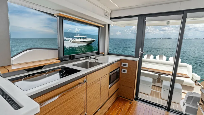 Slide: The Image of Galley and Aft Deck with Sea View This image showcases the sleek galley of the 2025 Tiara Yachts 48LE, featuring modern appliances and elegant wood cabinetry. The expansive windows provide a stunning view of the ocean, seamlessly connecting the indoors with the outdoor aft deck. The well- - 7403639