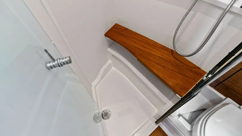 Slide: The Image of Elegant Yacht Bathroom with Teak Accents This well-appointed bathroom on the 2025 Tiara Yachts 48LE features a sleek shower with a luxurious teak bench, offering both comfort and style. The contemporary design is complemented by a chrome handheld shower fixture and a glass door, enhancing the mo - 7403658