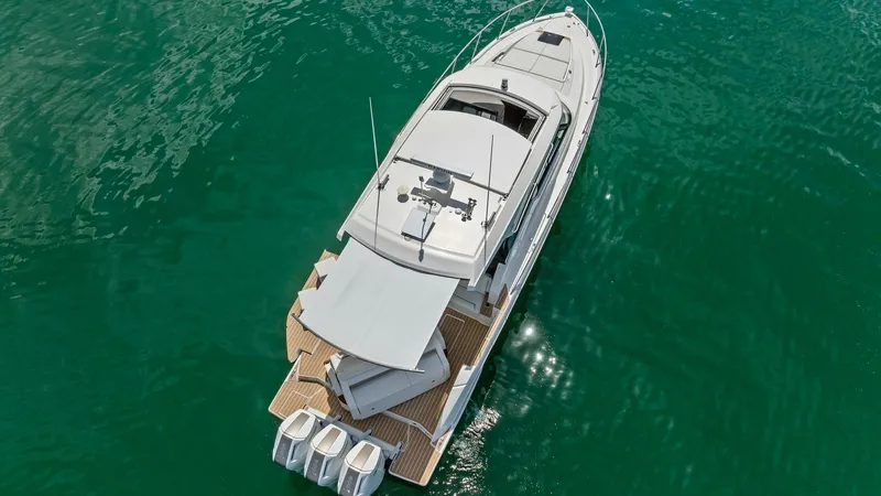 Slide: The Image of Aerial View of Aft Deck and Engines This aerial shot showcases the sleek and modern aft deck of the 2025 Tiara Yachts 48LE. The deck features elegant teak flooring, providing a luxurious contrast against the vibrant blue waters. Equipped with triple outboard engines, this vessel is designed - 7403598