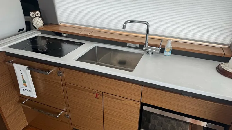 Slide: The Image of Galley with Modern Appliances The galley of the 2025 Tiara Yachts 48LE features sleek, modern cabinetry and high-end appliances, including an electric cooktop and stainless steel sink. The countertop provides ample space for meal preparation, while the built-in microwave and storage d - 7179505