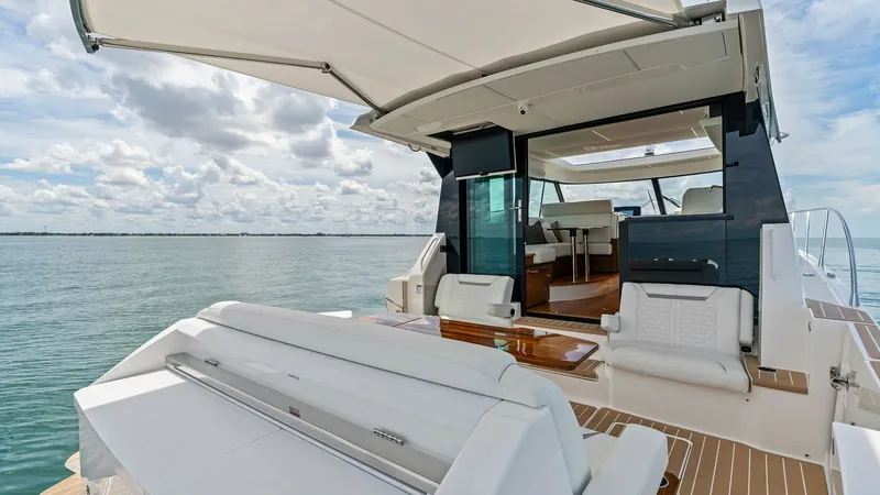 Slide: The Image of Spacious Aft Deck with Sunshade The aft deck of the 2025 Tiara Yachts 48LE features a luxurious seating area with plush, white upholstery, perfect for relaxation and entertainment. A retractable sunshade provides comfort from the sun, while the elegant teak decking adds a touch of sophi - 7403609