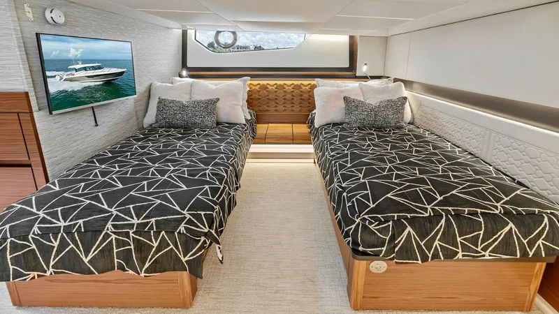 Slide: The Image of Twin Guest Stateroom with TV This inviting twin guest stateroom on the 2025 Tiara Yachts 48LE offers comfortable accommodations with two neatly arranged beds featuring modern geometric bedding. The room is equipped with a flat-screen TV, providing entertainment options, and a large w - 7403652