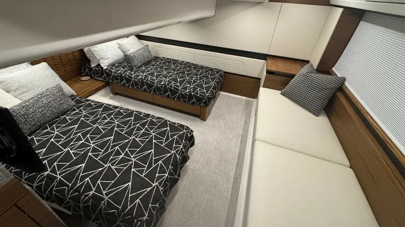 Slide: The Image of Guest Cabin with Twin Beds This elegant guest cabin on the 2025 Tiara Yachts 48LE features two stylish twin beds adorned with modern geometric-patterned bedding. The room is designed with warm wood finishes and soft ambient lighting, creating a cozy and inviting atmosphere. A plush - 7179506