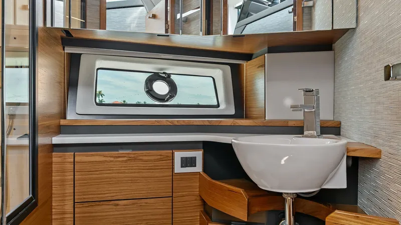 Slide: The Image of Modern Bathroom with Vanity This sleek bathroom features a contemporary vanity with elegant wood cabinetry and a stylish vessel sink. The room is well-lit, showcasing a large window with a porthole view, adding natural light and a nautical touch. The modern finishes and efficient la - 7403657