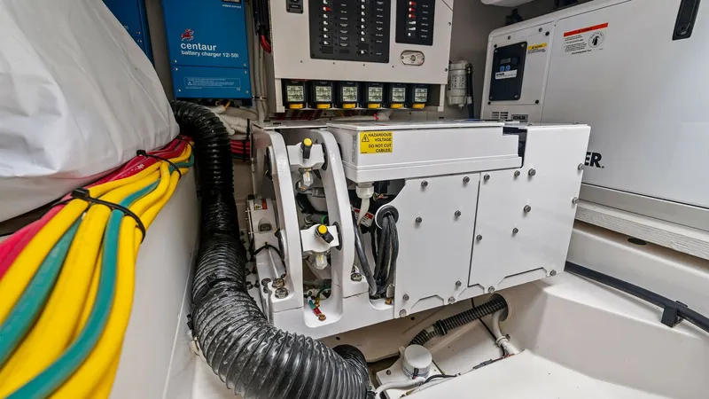 Slide: The Image of Engine Room with Electrical Systems This image showcases the engine room of the 2025 Tiara Yachts 48LE. Prominent features include a well-organized electrical panel with modern circuit controls and high-efficiency Victron Energy chargers. The area is neatly arranged with color-coded wiring - 7403664