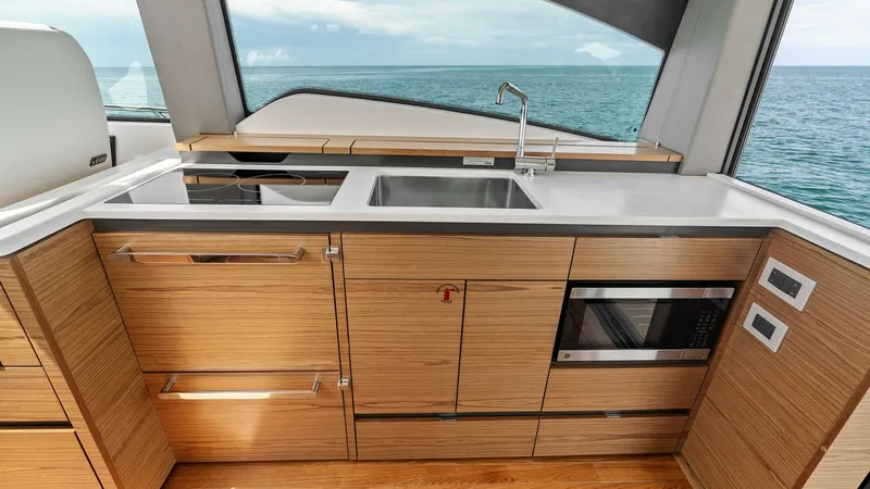 Slide: The Image of Modern Galley with Ocean View This sleek galley on the 2025 Tiara Yachts 48LE features elegant wood cabinetry and high-end appliances, including a built-in microwave. The expansive countertop provides ample workspace, complemented by a stainless steel sink. Large windows offer breatht - 7403626