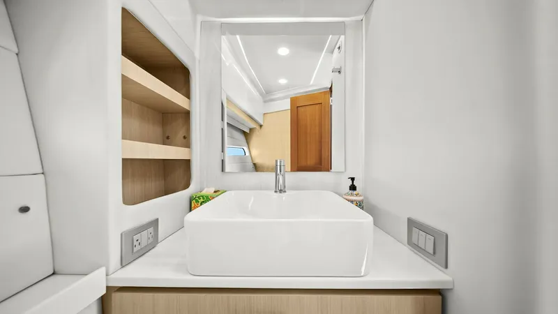 Slide: The Image of Modern Vanity in Ensuite Head This image showcases a sleek and modern vanity area in the ensuite head of the 2025 Regal 38 EXC. Featuring a contemporary square basin set atop a polished countertop, the space is complemented by open shelving for convenient storage. The warm wood finish - 7180441