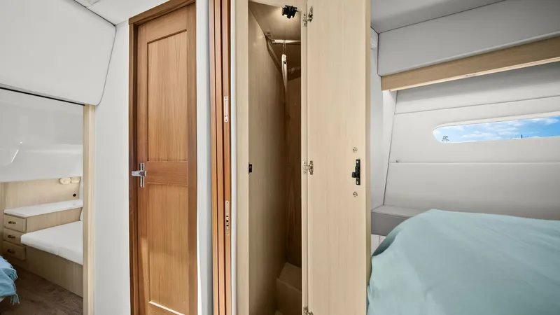Slide: The Image of Main Cabin Closet and Storage This image showcases the main cabin of the 2025 Regal 38 EXC, featuring a sleek wooden closet with ample storage space. The elegant wood finish complements the modern interior design, while the adjacent window allows natural light to enhance the cozy atmo - 7180438