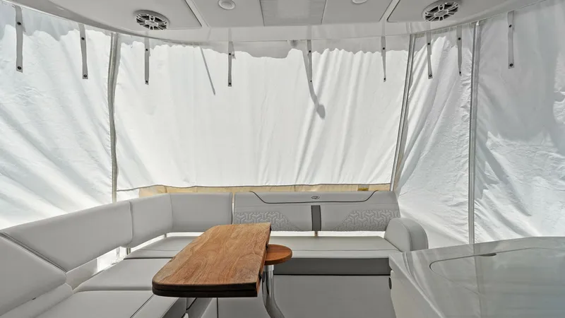 Slide: The Image of Enclosed Cockpit Lounge Area The enclosed cockpit of the 2025 Regal 38 EXC features a sleek, modern design with plush seating and a versatile wooden table, ideal for entertaining guests. The surrounding curtains provide privacy and protection from the elements, while the overhead spe - 7180426