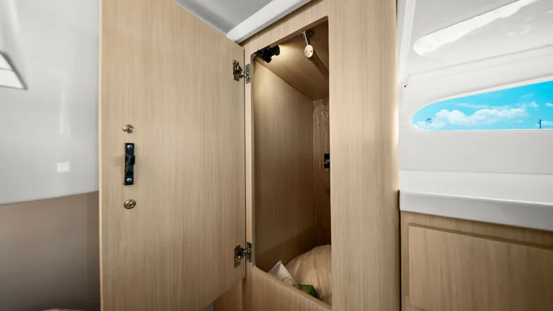 Slide: The Image of Cabin Wardrobe with Natural Light This image showcases the elegantly designed wardrobe within the cabin of the Regal 38 EXC. The light wood finish adds a modern touch, while the overhead lighting provides ample illumination. A nearby window floods the space with natural light, enhancing t - 7180447