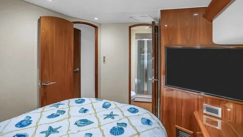 Slide: The Image of Guest Stateroom with Ensuite This inviting guest stateroom features a plush bed adorned with a nautical-themed bedspread, adding a touch of elegance to the space. Warm wooden finishes and soft ambient lighting create a cozy atmosphere, while the flat-screen TV offers entertainment op - 7224869