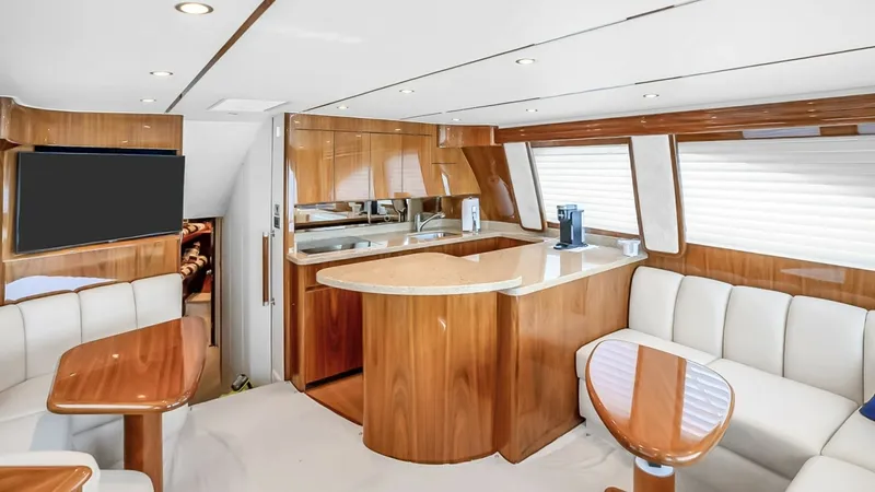 Slide: The Image of Spacious Salon with Galley This elegant salon of the 2021 Viking 48 Convertible boasts a luxurious blend of high-gloss wood finishes and plush seating. The open layout features a well-appointed galley with a polished countertop, ideal for entertaining. Large windows flood the space - 7224852