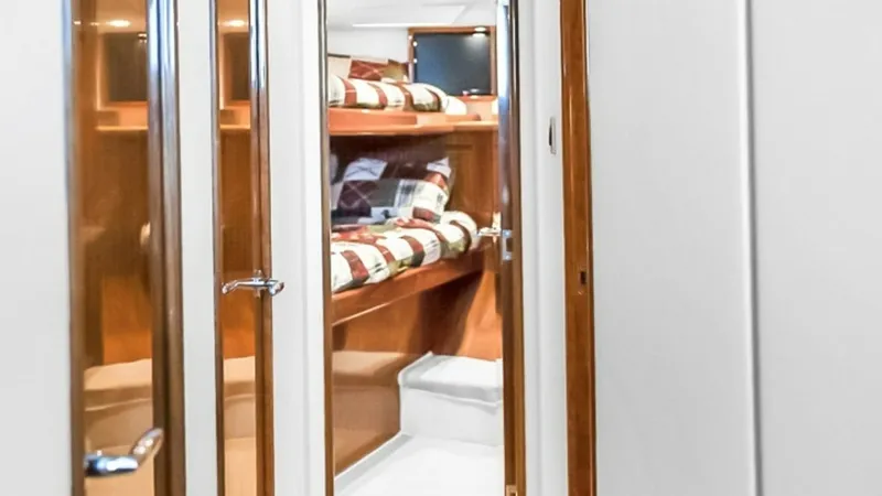 Slide: The Image of Hallway Leading to Guest Stateroom This bright and inviting hallway on the Viking 48 Convertible leads to a cozy guest stateroom. The space is enhanced by elegant wooden trim and modern recessed lighting. The stateroom features warm wood finishes and comfortable bunks, perfect for relaxing - 7224877
