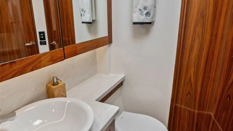 Slide: The Image of Elegant Enclosed Bridge Bathroom This image showcases the beautifully appointed bathroom of the 2021 Riviera 57 Enclosed Bridge. The space features a sleek white basin paired with rich wood cabinetry, creating a warm and inviting atmosphere. A large mirror and modern fixtures enhance the - 7541521