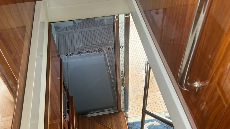 Slide: The Image of Stairway to Aft Deck This image showcases the elegant stairway leading to the aft deck of the 2021 Riviera 57 Enclosed Bridge. The rich wood finish and polished stainless steel handrails highlight the luxurious craftsmanship. Natural light floods this area, enhancing the invi - 7396157