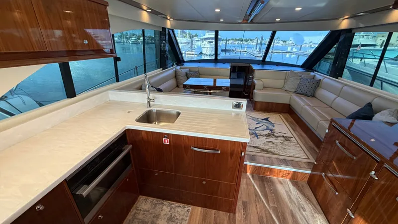 Slide: The Image of Spacious Salon with Galley View The salon of the 2021 Riviera 57 Enclosed Bridge showcases a luxurious and inviting setting, featuring large windows that offer panoramic views. The galley is elegantly equipped with high-quality appliances and a sleek countertop, seamlessly integrated in - 7396136