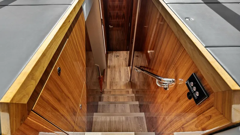 Slide: The Image of Interior Stairway to Lower Deck The stairway of the 2021 Riviera 57 Enclosed Bridge leads elegantly to the lower deck, showcasing exquisite wood finishes and modern design. The polished wooden steps and walls provide a warm, inviting atmosphere, complemented by sleek stainless steel han - 7541512