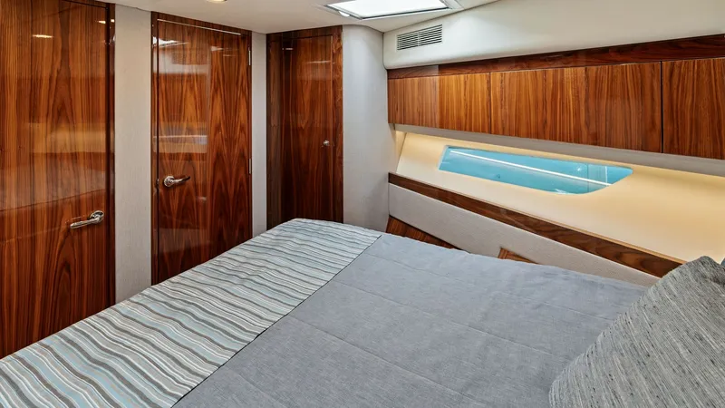 Slide: The Image of Luxurious Stateroom with Elegant Wood Finishes This inviting stateroom on the 2021 Riviera 57 Enclosed Bridge features exquisite wood paneling and a sleek, modern design. The large bed is complemented by ample natural light from the stylishly elongated window, creating a serene and comfortable retreat - 7541509