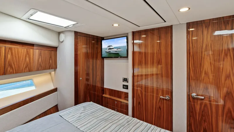 Slide: The Image of Luxurious Master Stateroom Interior The master stateroom of the 2021 Riviera 57 Enclosed Bridge exudes elegance with its rich wood finishes and modern design. A skylight provides natural light, enhancing the spacious feel, while the built-in entertainment system offers relaxation and conven - 7541511
