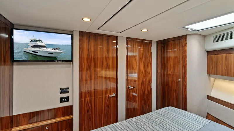Slide: The Image of Luxurious Stateroom with TV The stateroom of the 2021 Riviera 57 Enclosed Bridge exudes sophistication with its high-gloss wood cabinetry and modern fixtures. A wall-mounted flat-screen TV offers entertainment, while the ambient lighting creates a warm and inviting atmosphere. The r - 7541508