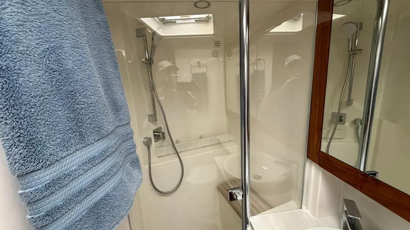 Slide: The Image of Modern Yacht Bathroom with Shower This sleek and modern bathroom aboard the 2021 Riviera 57 Enclosed Bridge features a spacious shower area with a rain-style showerhead. The elegant design includes a polished wood-framed mirror and a contemporary sink, enhancing the sophisticated ambiance - 7396152