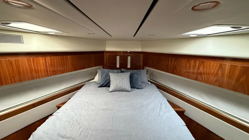 Slide: The Image of Forward Stateroom with Skylights The forward stateroom of the 2021 Riviera 57 Enclosed Bridge features a luxurious double bed framed by rich wooden cabinetry. Natural light pours in through dual skylights, enhancing the room's warm and inviting atmosphere. Clever storage solutions and el - 7396131