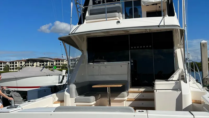 Slide: The Image of Aft Deck with Seating Area This image showcases the aft deck of the 2021 Riviera 57 Enclosed Bridge, featuring a comfortable seating area with a wooden table. The space is designed for relaxation and socializing, with ample seating and easy access to the main cabin. Its sleek desig - 7396158