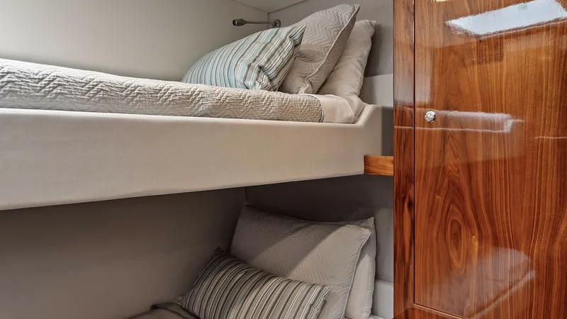 Slide: The Image of Guest Cabin with Twin Bunks This cozy guest cabin on the 2021 Riviera 57 Enclosed Bridge features comfortable twin bunk beds, perfect for additional guests. The elegant wood finishes add a touch of warmth and sophistication, while ample storage space ensures functionality. Soft ligh - 7541514