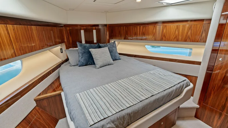 Slide: The Image of Luxurious Forward Stateroom This inviting forward stateroom on the 2021 Riviera 57 Enclosed Bridge features a plush double bed accented by rich wooden cabinetry and sleek design. Large windows provide ample natural light and offer a serene view of the sea, creating a tranquil retrea - 7541506