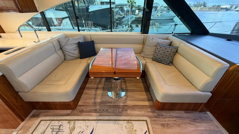 Slide: The Image of Salon Seating Area with Panoramic Views This inviting salon on the 2021 Riviera 57 Enclosed Bridge features plush L-shaped seating with elegant, cream-colored upholstery. The wooden table is a focal point, offering a perfect spot for dining or socializing while enjoying expansive views through - 7396134