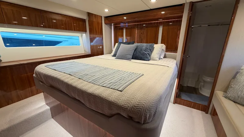 Slide: The Image of Master Stateroom with Ensuite The master stateroom of the 2021 Riviera 57 Enclosed Bridge offers a luxurious retreat with a spacious bed and elegant wood finishes. Natural light floods through the large window, enhancing the room's airy ambiance. The ensuite bathroom is conveniently a - 7396147
