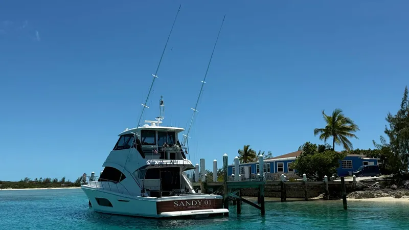 Slide: The Image of Aft View at Dock This image showcases the sleek aft view of the 2021 Riviera 57 Enclosed Bridge, perfectly moored at a picturesque dock. The vessel's elegant lines and enclosed bridge design are highlighted against the backdrop of clear turquoise waters and tropical scene - 7396161