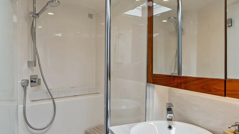 Slide: The Image of Luxurious Enclosed Bathroom This elegant bathroom on the 2021 Riviera 57 Enclosed Bridge features a modern, sleek design with high-gloss wooden accents and a pristine white finish. The spacious shower area is equipped with a stylish, handheld showerhead and contemporary fixtures. Am - 7541517