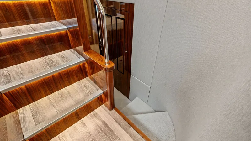 Slide: The Image of Staircase with Ambient Lighting This image showcases the stylish staircase of the 2021 Riviera 57 Enclosed Bridge, featuring elegant wood finishes and ambient lighting. The steps are crafted with high-quality materials, offering both durability and aesthetic appeal. A sleek stainless st - 7541505