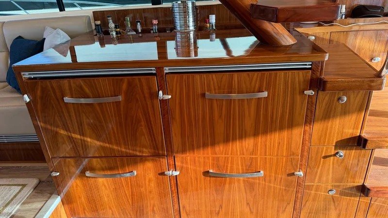 Slide: The Image of Galley Storage and Bar Area This image showcases the elegant galley storage and bar area of the 2021 Riviera 57 Enclosed Bridge. The cabinetry is crafted from high-gloss wood, providing a luxurious touch and ample storage space. Sleek stainless steel handles complement the rich wood - 7396140