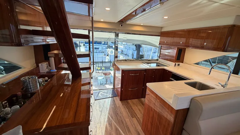 Slide: The Image of Galley and Salon Entrance View This image showcases the stylish galley of the 2021 Riviera 57 Enclosed Bridge, featuring high-gloss wood cabinetry and modern appliances. The sleek countertops and ample storage space offer functionality and elegance. Natural light floods the area throug - 7396138