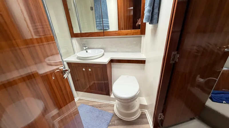 Slide: The Image of Luxury Ensuite Bathroom Interior The Riviera 57 Enclosed Bridge features a luxurious ensuite bathroom with high-gloss wood cabinetry and modern fixtures. The space includes a stylish countertop with an integrated sink, complemented by a large mirrored cabinet for ample storage. The elega - 7396148