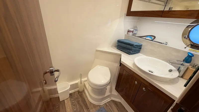 Slide: The Image of Elegant Onboard Bathroom This onboard bathroom of the 2021 Riviera 57 Enclosed Bridge boasts a sleek design with rich wooden cabinetry and a stylish basin. The space is efficiently utilized, featuring a modern toilet and ample storage behind mirrored cabinets. The warm lighting a - 7396151