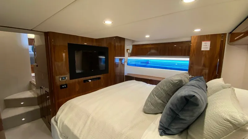 Slide: The Image of Luxurious Master Stateroom Interior The master stateroom of the 2021 Riviera 57 Enclosed Bridge exudes comfort and elegance with its plush bedding and modern finishes. Rich wood paneling complements the sleek, mounted flat-screen TV, creating a sophisticated ambiance. Ample natural light fi - 7396149