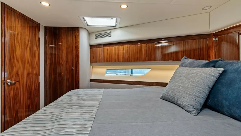 Slide: The Image of Luxurious Forward Stateroom This inviting forward stateroom features a plush queen-sized bed with elegant bedding, complemented by rich wooden cabinetry. Natural light streams through the side window, enhancing the room's warm ambiance, while recessed lighting adds a touch of sophis - 7541507