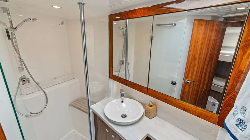 Slide: The Image of Luxurious Yacht Bathroom Suite This elegant bathroom on the 2021 Riviera 57 Enclosed Bridge features a spacious shower with a sleek glass enclosure. The vanity area is equipped with a modern sink, polished wood cabinetry, and a large mirror, creating a sophisticated and functional spac - 7541518