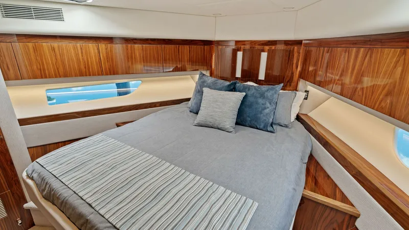 Slide: The Image of Luxurious Forward Stateroom The forward stateroom of the 2021 Riviera 57 Enclosed Bridge features elegant wood paneling and a plush queen-sized bed, offering a cozy retreat. Ample natural light floods through the side windows, enhancing the warm tones of the high-quality finishes. D - 7541510