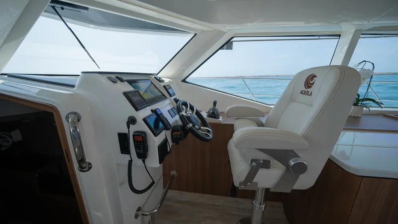 Slide: The Image of Helm Station with Captain's Chair The helm station of the 2021 Aquila 44 CAT features a sleek, modern design with state-of-the-art navigation equipment neatly integrated into the console. The plush captain's chair, embroidered with the Aquila logo, offers comfort and style, complemented b - 7413977