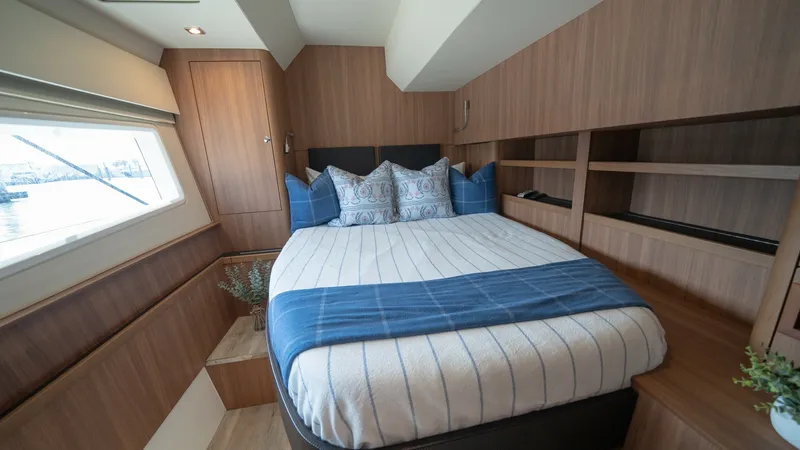 Slide: The Image of Forward Stateroom with Queen Bed This inviting forward stateroom features a plush queen-sized bed adorned with elegant bedding, offering a restful retreat. The warm wood paneling and built-in shelving create a cozy yet functional atmosphere, while large windows provide ample natural ligh - 7413965