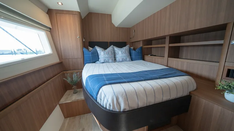 Slide: The Image of Forward Cabin with Double Berth The forward cabin of the Aquila 44 CAT features a spacious double berth with stylish striped bedding and plush pillows, creating a cozy retreat. Rich wood paneling and built-in shelving add elegance and functionality, offering ample storage for personal i - 7413961