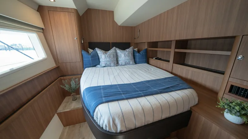 Slide: The Image of Guest Cabin with Queen Bed This inviting guest cabin on the Aquila 44 CAT features a comfortable queen-sized bed adorned with elegant blue and white linens. The room is accented with rich wood paneling and ample built-in shelving, offering both style and storage. Large windows floo - 7413963