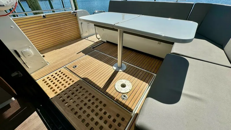 Slide: The Image of Aft Deck with Seating Area This Beneteau Antares 11 features a spacious aft deck with stylish teak flooring, offering a perfect space for socializing and relaxation. The comfortable L-shaped seating wraps around a sleek, adjustable table, ideal for dining or enjoying the view. The - 7403692