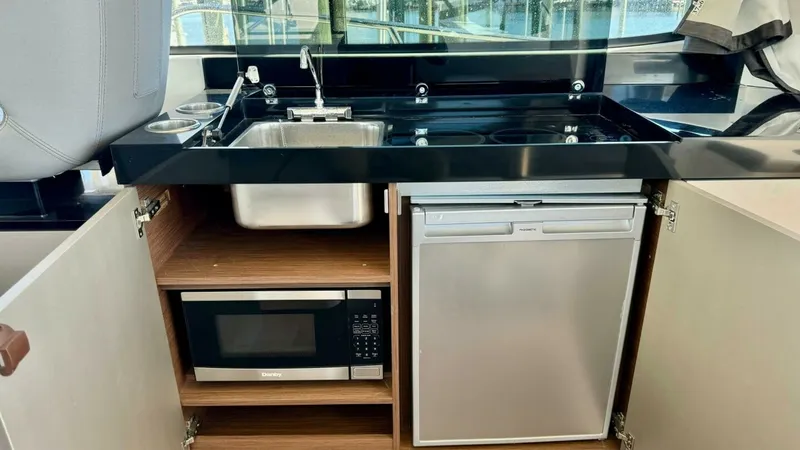 Slide: The Image of Galley with Sink and Appliances The galley of the 2022 Beneteau Antares 11 showcases a compact yet efficient layout, featuring a sleek stainless steel sink and a modern stovetop set into a glossy black countertop. Below, a microwave and a compact refrigerator are neatly integrated into - 7403680