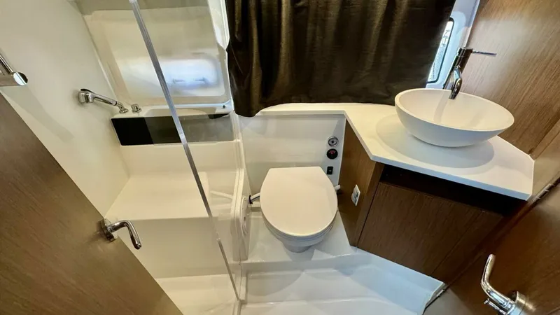 Slide: The Image of Modern En-Suite Bathroom This well-appointed en-suite bathroom aboard the 2022 Beneteau Antares 11 features a sleek, contemporary design. It includes a stylish vessel sink atop a wooden vanity, complemented by a modern, enclosed shower area. The space is efficiently arranged to m - 7403687